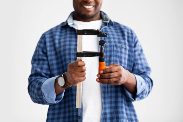 Černé mužské ruce drží stavební nástroj svorka, připraven k opravě doma, stojící na bílém pozadí nástěnného studia - Fotografie, Obrázek