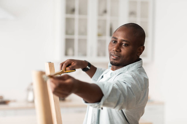 Africano americano faz-tudo trabalhando em casa, medindo a largura entre as pernas da mesa de madeira, montagem de móveis - Foto, Imagem