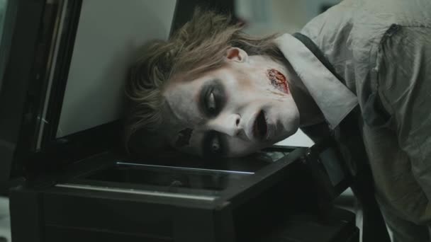 Medium shot of zombie man with SFX makeup and fake wounds grunting and photocopying his face on copier - Footage, Video