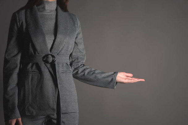 Woman in the suit is showing on the copy space on the gray background. Product presentation. - Foto, Imagen