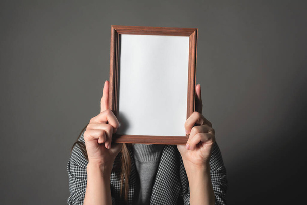 Diploma or certificate mockup. Woman is hiding her face behind an empty photo frame border on a gray background. - Foto, Imagem
