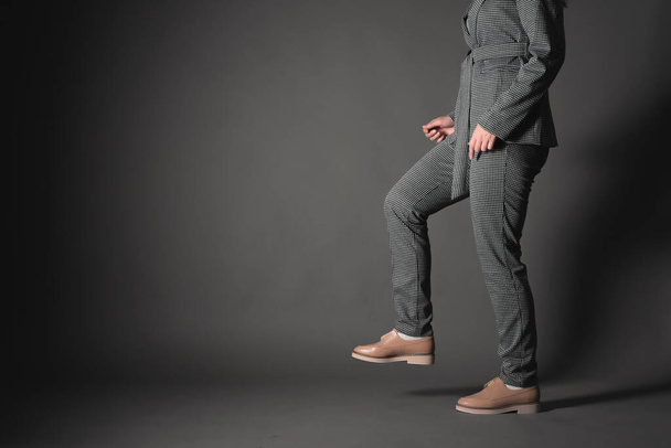 Woman in the gray suit and shoes steps on the gray background with copy space. Side view. - Foto, Imagem