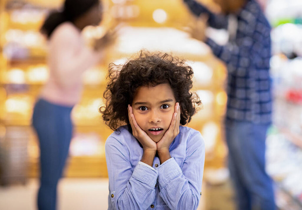 Little black girl feeling shocked while her parents arguing at big shopping mall - Fotografie, Obrázek