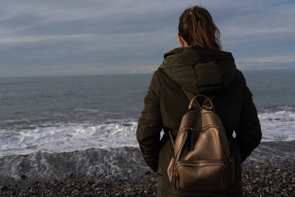Девушка с рюкзаком гуляет по пляжу зимой - Фото, изображение