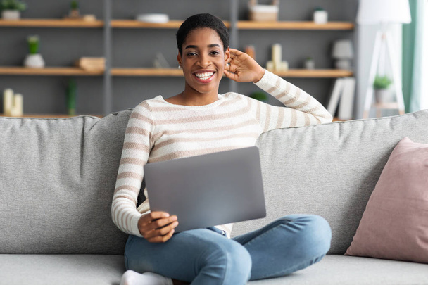 Op afstand werken. Portret van gelukkig zwart vrouw zitten op bank met laptop - Foto, afbeelding