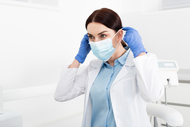 dentista em luvas de látex usando máscara médica na clínica odontológica  - Foto, Imagem