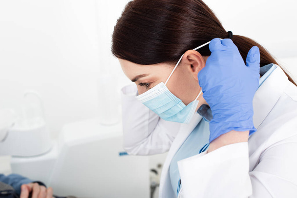 Diş kliniğinde tıbbi maske takan lateks eldivenli esmer dişçi. - Fotoğraf, Görsel