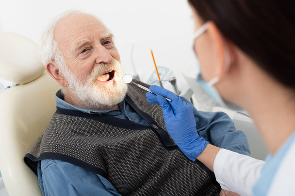vanhempi mies, jolla on hammaslääkärin suorittama hammastarkastus lateksikäsineissä peili hammastuolissa - Valokuva, kuva