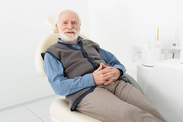uomo anziano seduto con le mani serrate in sedia dentale in clinica - Foto, immagini