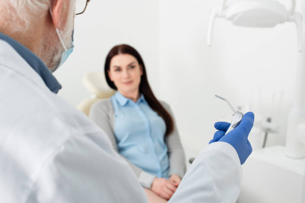 dentista sênior com equipamento médico na mão na frente do paciente na cadeira dental - Foto, Imagem