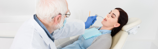 Oberzahnarzt in medizinischer Maske, die Zahnbehandlung der attraktiven Frau im Zahnarztstuhl macht, Banner - Foto, Bild