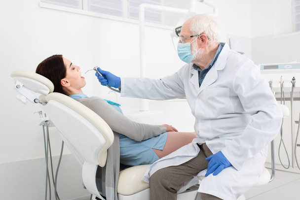 старший стоматолог в медичній масці лікування зубів пацієнта в стоматологічному кріслі
 - Фото, зображення