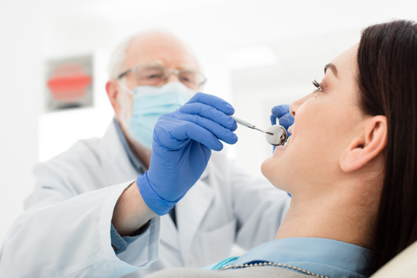старший стоматолог вивчає зуби дорослої жінки з зондом і дзеркалом в стоматологічній клініці
 - Фото, зображення
