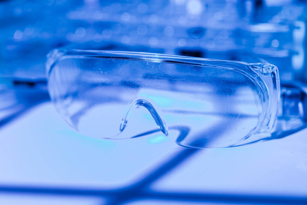Óculos de proteção do pesquisador cientista em uma mesa de laboratório, com ambiente de luz azul - Foto, Imagem