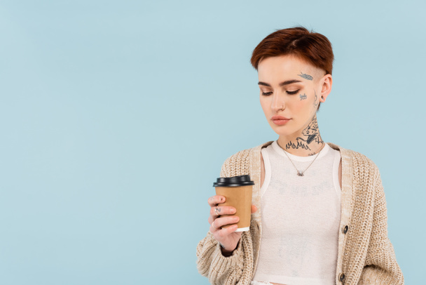 young tattooed woman holding paper cup isolated on blue  - Foto, Imagem