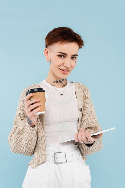cheerful young woman with tattoos holding digital tablet and paper cup isolated on blue - Fotoğraf, Görsel