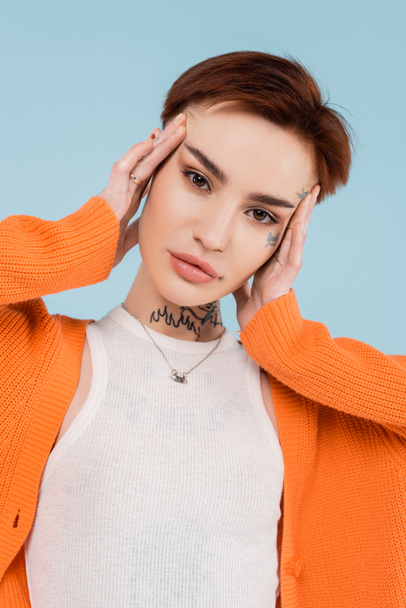 young woman with tattoos in orange cardigan posing isolated on blue - Foto, afbeelding