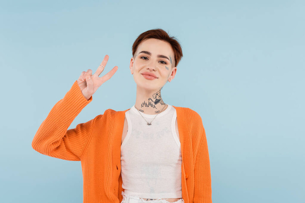 happy young woman with tattoos showing peace sign isolated on blue - Photo, Image