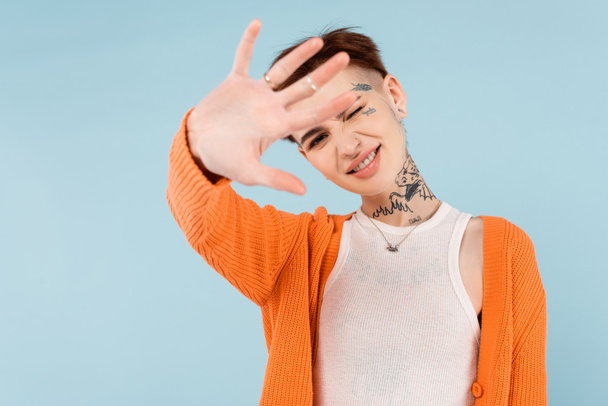 happy young tattooed woman in orange cardigan showing stop gesture isolated on blue - Фото, зображення