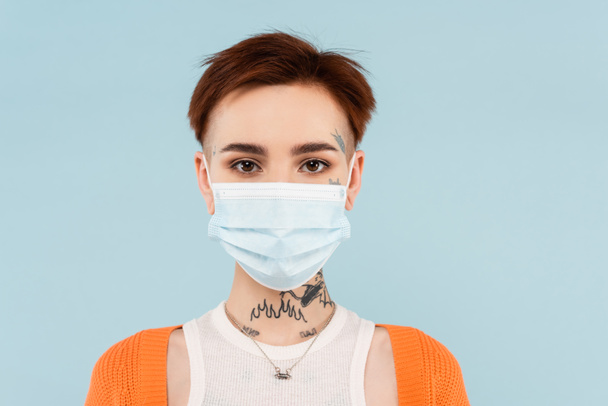 young tattooed woman in orange cardigan and medical mask isolated on blue - Photo, Image