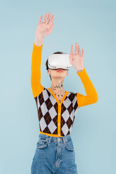 young tattooed woman in vr headset gesturing isolated on blue - Zdjęcie, obraz