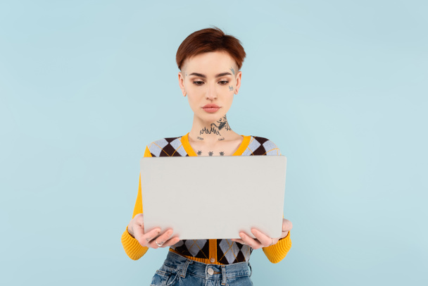 young and tattooed freelancer using laptop isolated on blue - Fotografie, Obrázek
