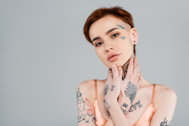 young tattooed woman looking at camera isolated on grey  - Фото, зображення