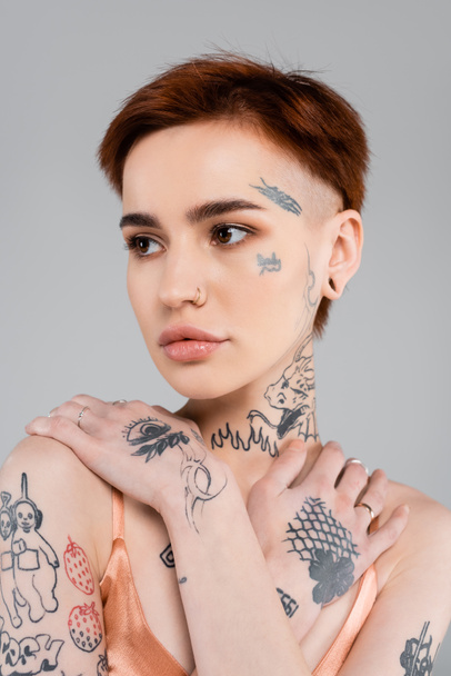 fiatal nő tetoválásokkal néz félre elszigetelt szürke  - Fotó, kép