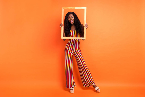 Full length photo of dark skin happy amazed woman hold wooden frame picture isolated on orange color background - Фото, зображення