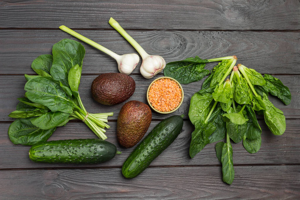 Avocado, red lentils, and garlic. Spinach leaves and cucumbers on table. Dark wooden background. Flat lay - Photo, Image
