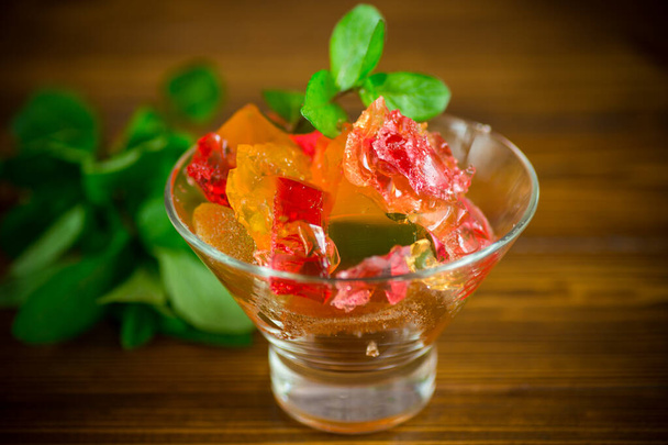 colored sweet fruit jelly in a glass glass on a wooden table - Foto, afbeelding
