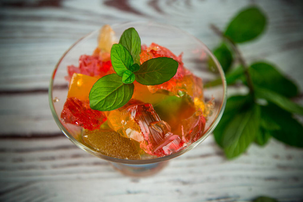 colored sweet fruit jelly in a glass glass on a wooden table - Foto, afbeelding