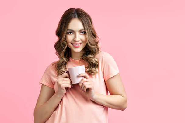 Smiling pretty woman enjoying cup of aroma coffee on pink background - Zdjęcie, obraz