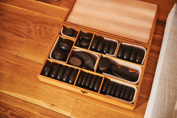 Pudełko z czarnymi kamieniami do masażu leżące na podłodze - Zdjęcie, obraz