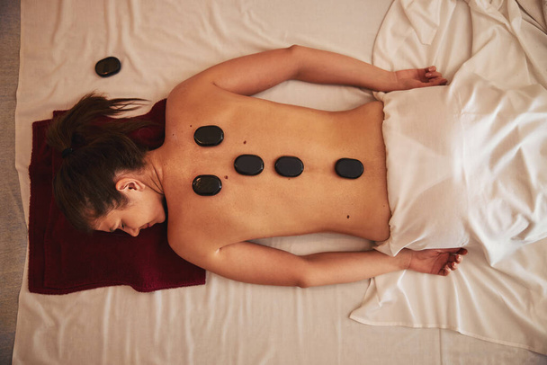 Pedras de massagem quente cobrindo omoplatas e coluna vertebral de fêmea - Foto, Imagem