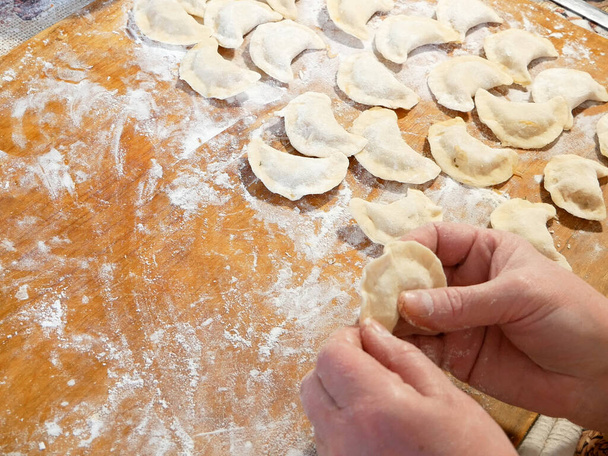 process of making homemade dumplings, ravioli or pelmeni with vegetables filling. Ready for cooking raviolis on wooden board, woman hand holds one, closeup - 写真・画像
