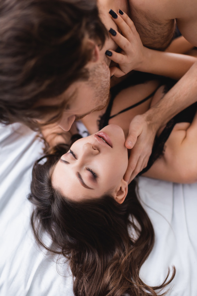 Blurred man touching sensual girlfriend with closed eyes on bed  - Photo, Image