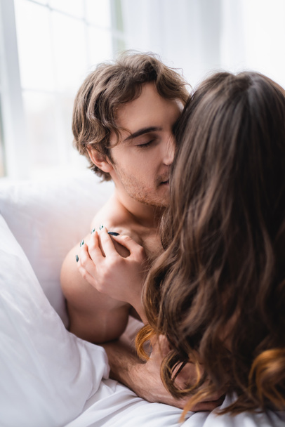 Young man kissing brunette girlfriend on bed  - Photo, Image