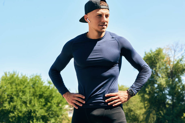 Image of an athlete male in sportswear with hands on the waist posing before the workout on a sunny day outdoors. Portrait of an athletic man taking a break after exercising in the park.  - Valokuva, kuva