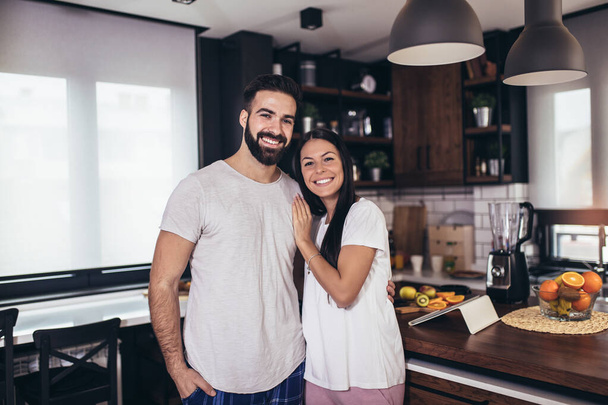 Jovem casal feliz posando na cozinha moderna enquanto prepara o café da manhã. - Foto, Imagem