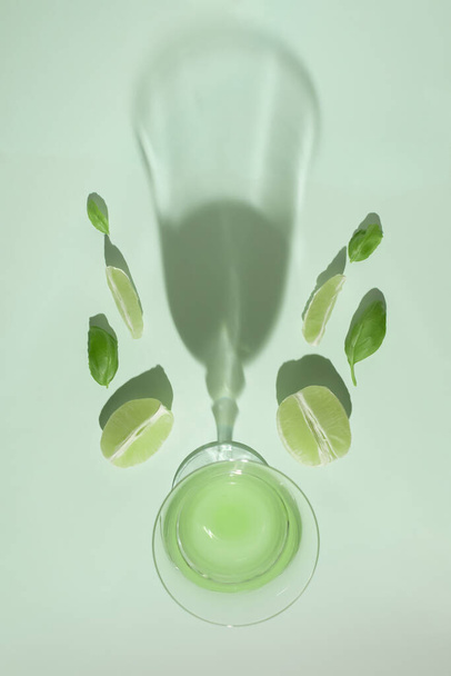 Idée de fruits d'été minimaliste rétro avec un verre à boire, des feuilles d'herbes vertes et du citron vert bio pelé. Concept d'alimentation saine, design plat. - Photo, image