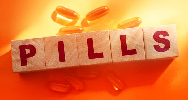Pills word on wooden cubes with oil capsuless around on orange background. Medical healthcare concept. - Foto, Imagem