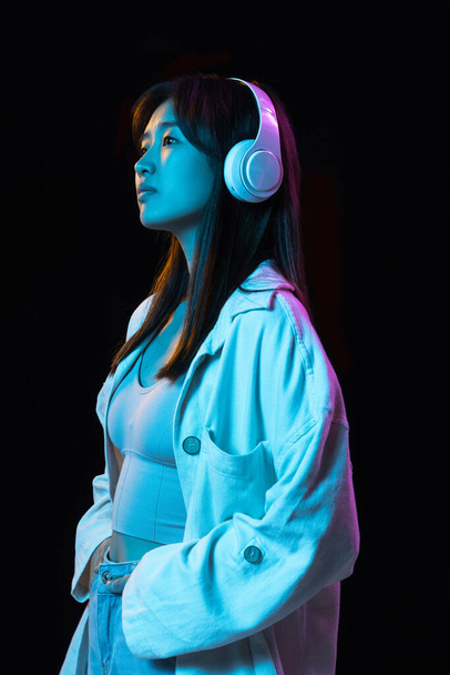 Aziatische jonge vrouwen portret op donkere studio achtergrond in neon. Concept van menselijke emoties, gezichtsuitdrukking, jeugd, verkoop, reclame. - Foto, afbeelding