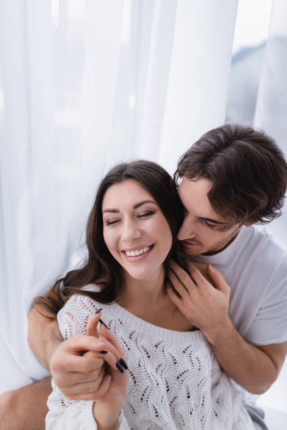 Young man embracing and holding hand of cheerful girlfriend with closed eyes - Photo, Image
