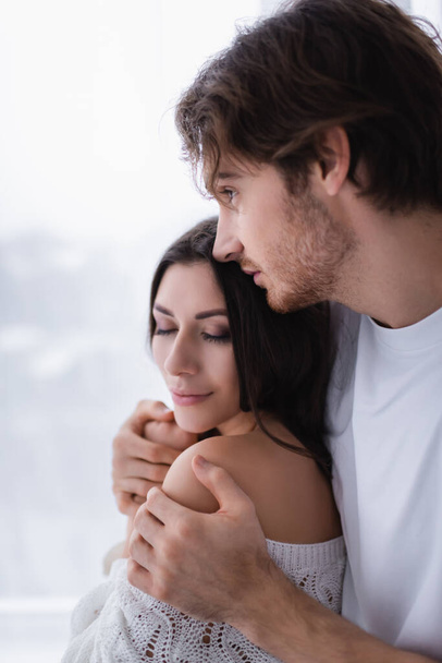 Man embracing brunette girlfriend with closed eyes at home  - Fotó, kép