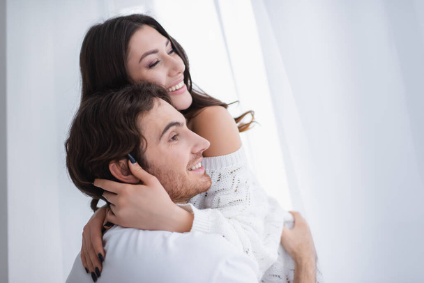 Smiling man hugging girlfriend at home  - Foto, afbeelding