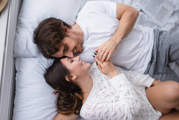 Top view of man smiling while lying on bed with girlfriend  - Foto, imagen