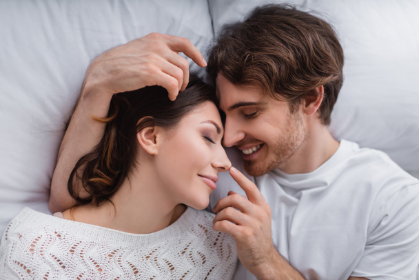 Widok z góry uśmiechnięty mężczyzna dotykając nosa dziewczyny na łóżku  - Zdjęcie, obraz