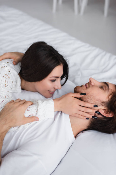 Hymyilevä nainen koskettaa kaulan poikaystävä sängyssä  - Valokuva, kuva