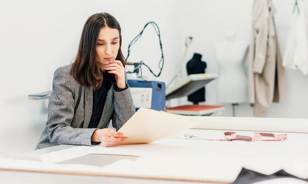 Horizontal image of a owner fashion female designer looking on the sketch for new collection. Businesswoman working on a new garment for an online store in her creative office. - Фото, зображення